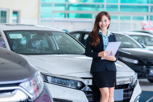 Jovem mulher asiática em um conceito do assistente de serviço do aluguer de carros / vendas carro na sala de exposições