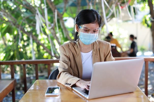 Jovem mulher asiática em vestido casual com protetor facial e máscara protetora para cuidados de saúde