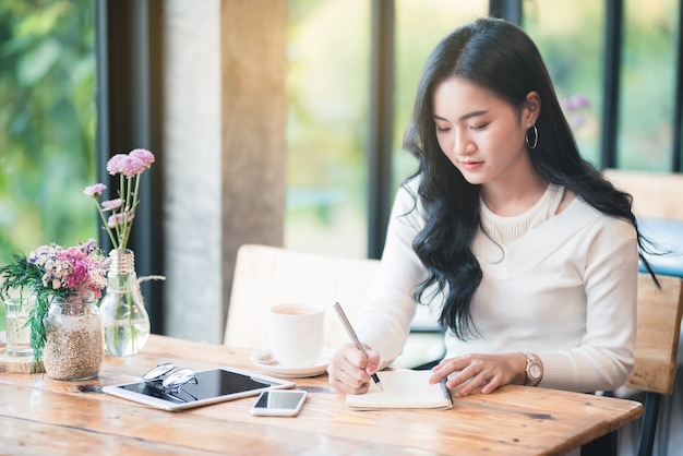 Jovem mulher asiática escrevendo notas no café