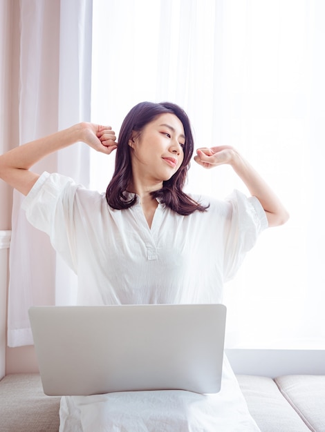Jovem mulher asiática, esticando os braços depois de usar o laptop.
