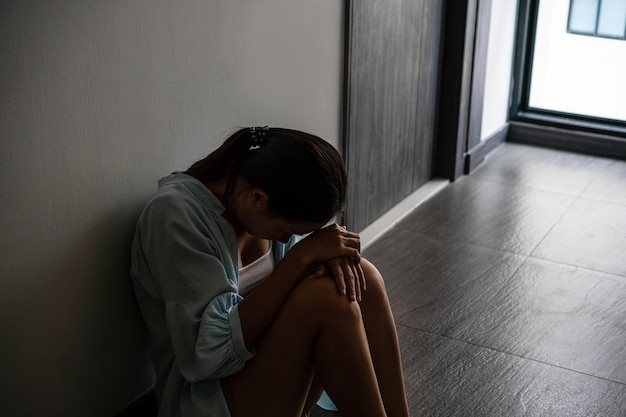 Jovem mulher asiática estressada sofrendo de depressão e sentada sozinha do lado de fora da sala ou corredor do apartamento Triste infeliz decepcionado abuso doméstico ou parar a violência e o conceito de estupro Espaço para texto