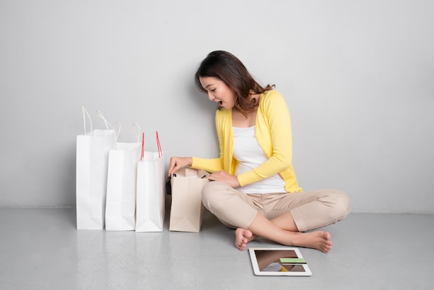 Jovem mulher asiática fazendo compras on-line em casa sentada ao lado da fileira de sacolas de compras