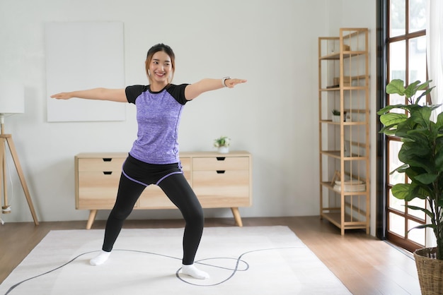 Jovem mulher asiática fazendo exercícios de equilíbrio de ioga com pose de guerreiro para um estilo de vida saudável em casa