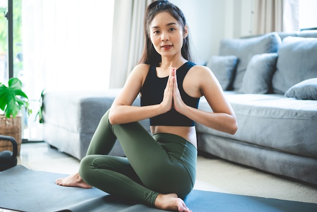 Jovem mulher asiática fazendo exercícios de ioga na academia em casa, estilo de vida feminino saudável com treinamento esportivo fitness em casa, garota fazendo exercícios físicos ativos no corpo, quarto interno da casa, relaxamento e bem-estar