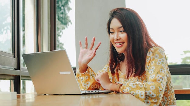 Foto jovem mulher asiática fazendo videoconferência no computador portátil enquanto está sentada no café tendo reunião