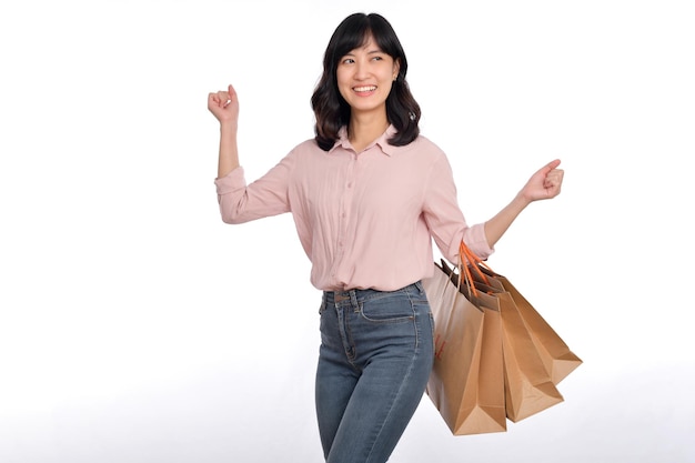 Jovem mulher asiática feliz com camisa casual e jeans segurando saco de papel comercial isolado no fundo branco