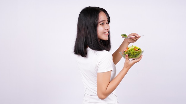 Jovem mulher asiática feliz comendo uma salada saudável com uma superfície branca isolada