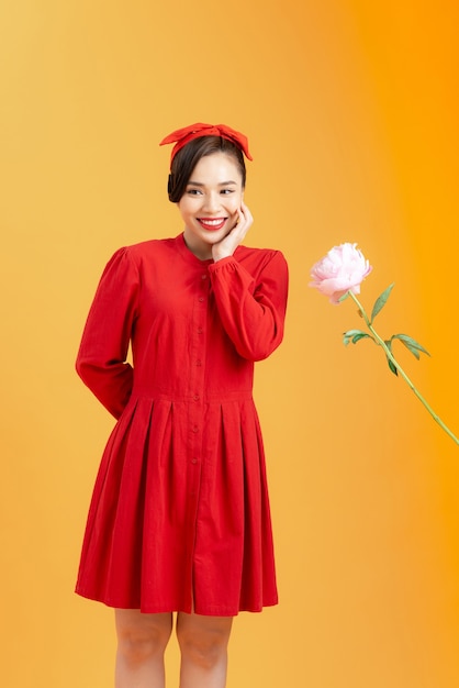 Jovem mulher asiática feliz em receber peônia rosa quando em pé isolado em um fundo laranja.