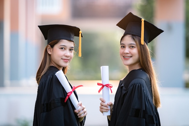 Jovem mulher asiática feliz, graduada em vestido de formatura e cartolina, possui um certificado de graduação para comemorar a conquista da educação no campus da universidade. foto de estoque de educação