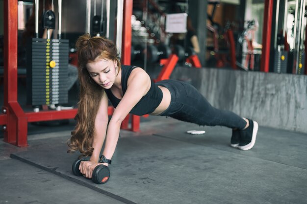 jovem mulher asiática fitness exercício e fazendo posição de prancha com halteres