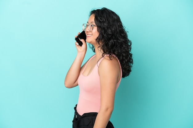 Jovem mulher asiática isolada em um fundo azul conversando com o celular