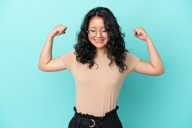 Jovem mulher asiática isolada em um fundo azul fazendo um gesto forte