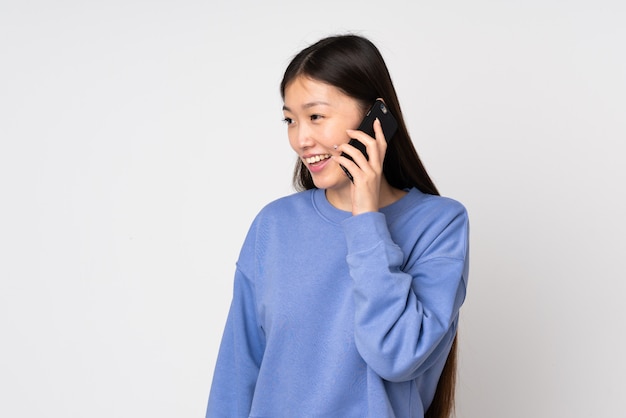 Jovem mulher asiática isolada na parede, mantendo uma conversa com o telefone móvel com alguém