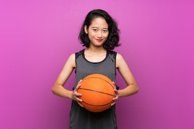 Jovem mulher asiática jogando basquete na parede roxa isolada