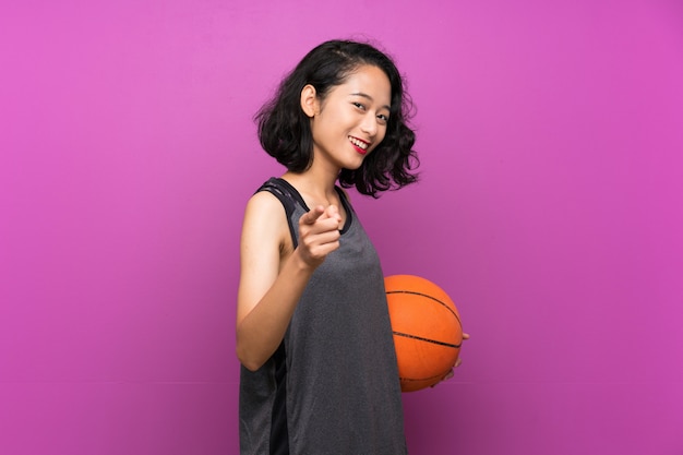Jovem mulher asiática jogando basquete na parede roxa isolada