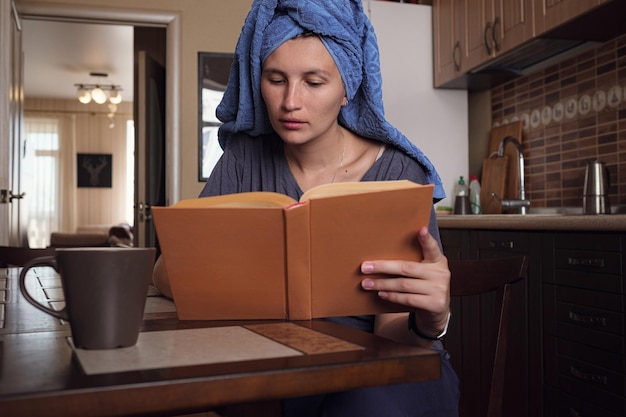 Jovem mulher asiática lê um livro na cozinha