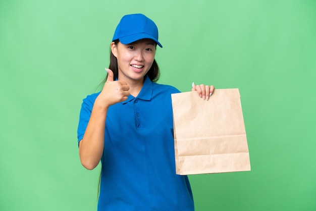 Jovem mulher asiática levando um saco de comida para viagem sobre fundo isolado com polegares para cima porque algo de bom aconteceu