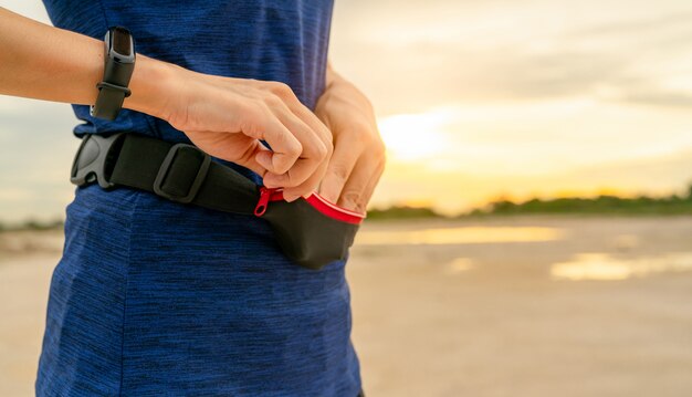 Jovem mulher asiática mantenha o smartphone na bolsa da cintura antes de executar o exercício cardio de manhã.