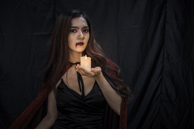 Foto jovem mulher asiática na fantasia de bruxa e segurar a vela no fundo de pano preto do conceito de halloween. retrato de mulher adolescente vestida de bruxa para celebrar o festival de halloween.