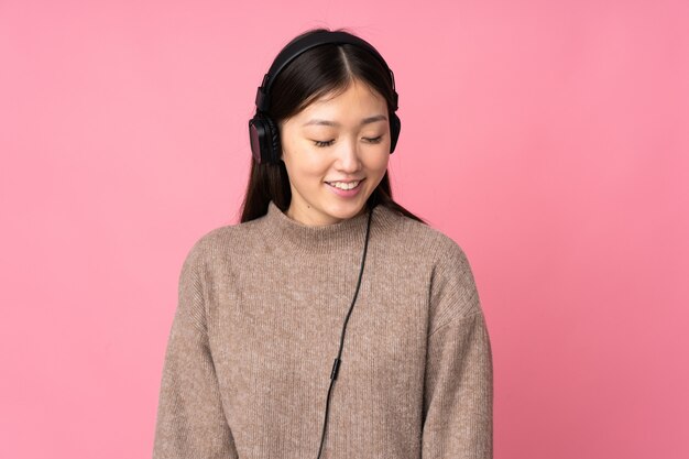 Jovem mulher asiática na parede rosa ouvindo música