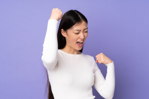 Jovem mulher asiática na parede roxa, comemorando uma vitória