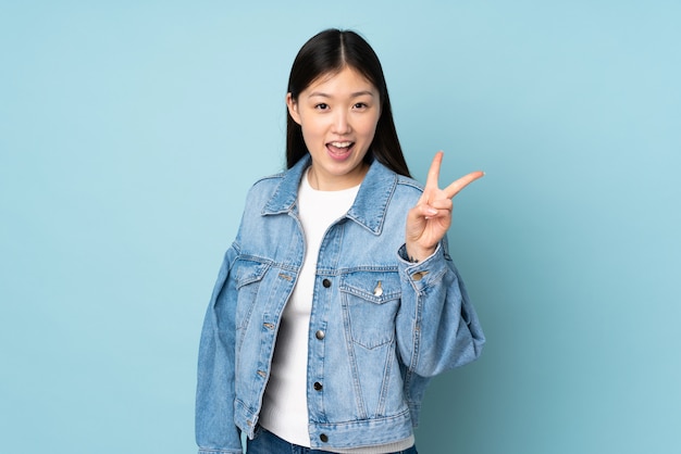 Jovem mulher asiática na parede, sorrindo e mostrando sinal de vitória