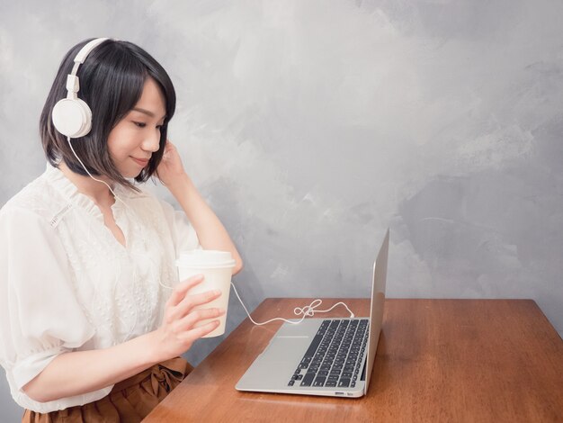 Jovem mulher asiática ouvindo fones de ouvido na frente do laptop