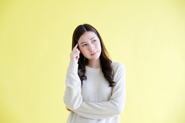 Foto jovem mulher asiática pensando em pé sobre fundo amarelo isolado