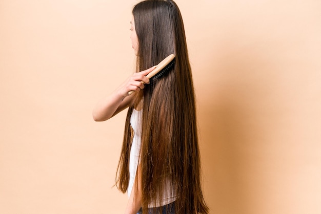 Jovem mulher asiática penteando o cabelo isolado em fundo bege