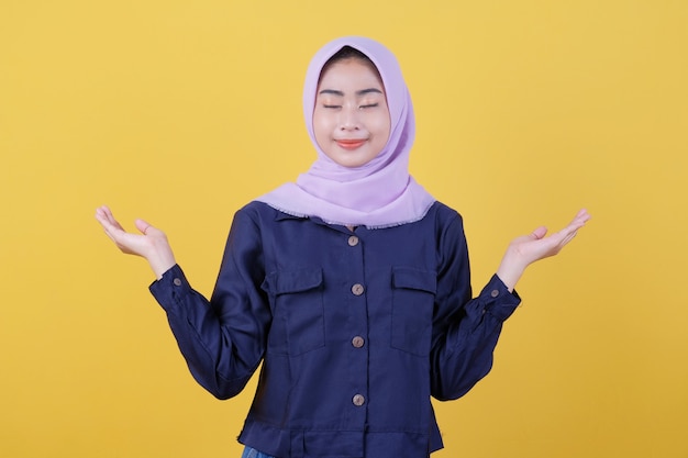 Foto jovem mulher asiática que é positiva com um sorriso alegre no rosto, vestindo um hijab e roupas casuais na sala é amarela. feche os olhos dela