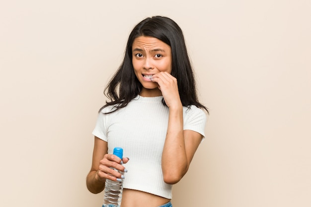 Jovem mulher asiática segurando as unhas cortantes de uma garrafa de água, nervosa e muito ansiosa.