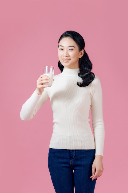 Jovem mulher asiática segurando leite com sorriso no fundo rosa