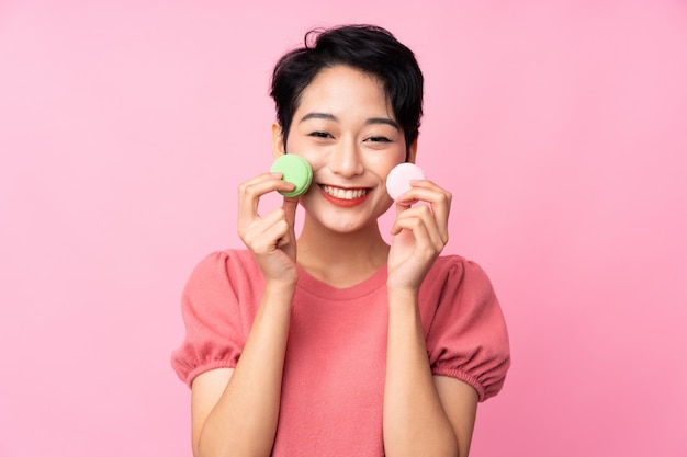 Jovem mulher asiática segurando macarons franceses coloridos e sorrindo