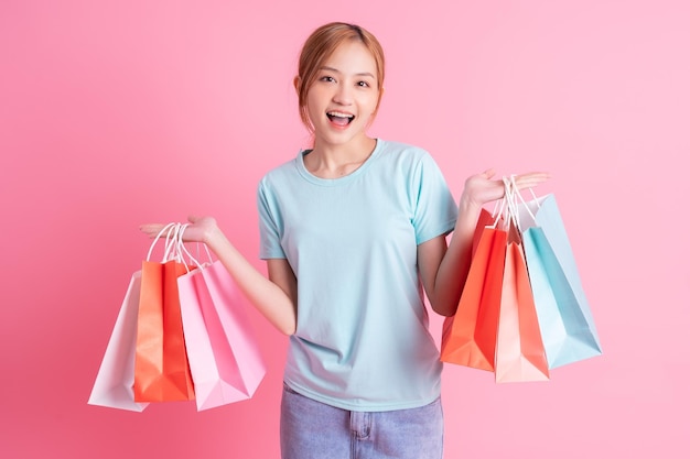 Jovem mulher asiática segurando sacola de compras no fundo rosa