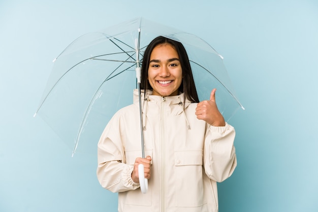 Jovem mulher asiática segurando um guarda-chuva, sorrindo e levantando o polegar