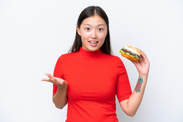 Jovem mulher asiática segurando um hambúrguer isolado no fundo branco com expressão facial chocada