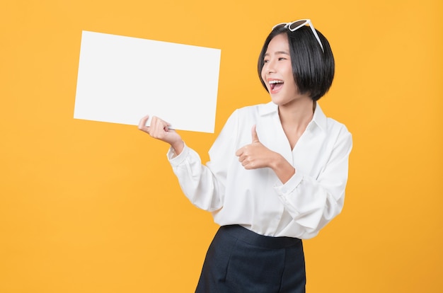 Jovem mulher asiática segurando um papel em branco com uma cara sorridente e olhando para o fundo laranja. para cartazes publicitários.