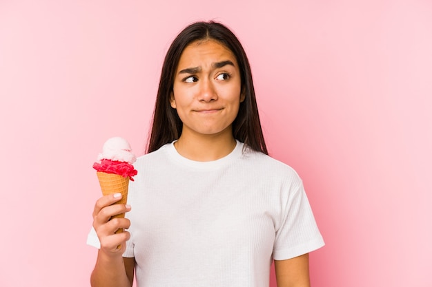 Jovem mulher asiática segurando um sorvete isolado confusa, sente-se em dúvida e insegura.