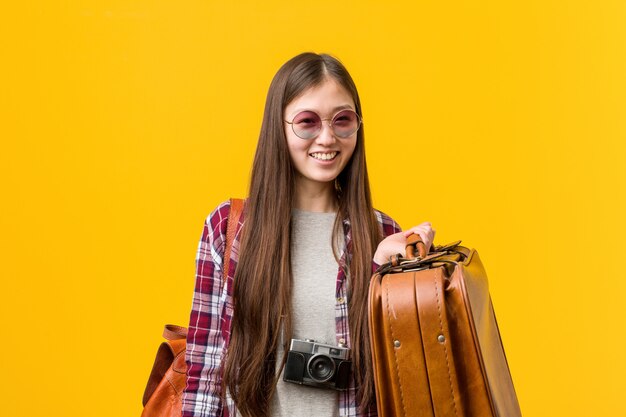 Jovem mulher asiática segurando uma mala feliz, sorridente e alegre.