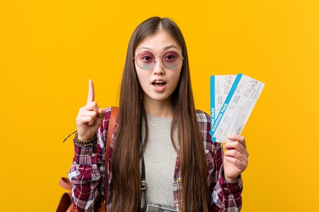 Jovem mulher asiática segurando uma passagem aérea, tendo uma ótima idéia