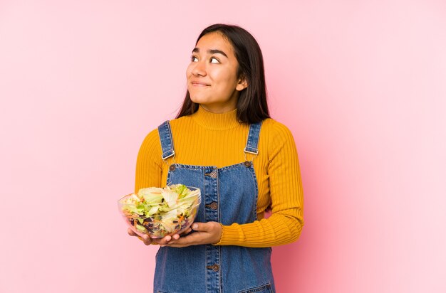 Jovem mulher asiática segurando uma salada isolada, sonhando em alcançar objetivos e propósitos