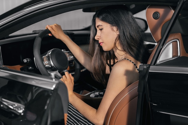 Jovem mulher asiática sentada em um carro de luxo na garagem antes de ligar o motor