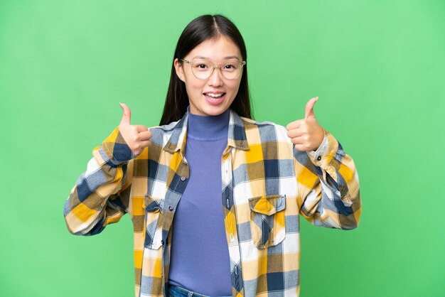 Jovem mulher asiática sobre fundo chave de croma isolado, dando um polegar para cima gesto