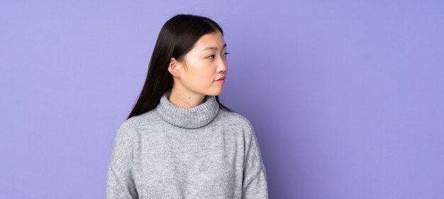 Jovem mulher asiática sobre parede isolada, olhando para o lado