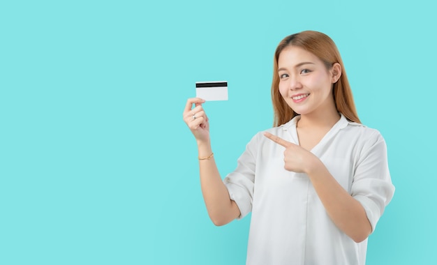 Jovem mulher asiática sorridente, apontando o dedo no cartão de crédito em branco