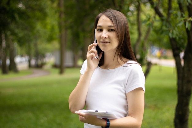 Jovem mulher asiática sorridente falando no celular, em um escritório moderno com um documento nela