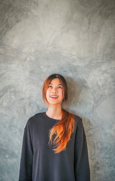 Jovem mulher asiática sorrindo retrato na frente de uma parede de cimento cinza.