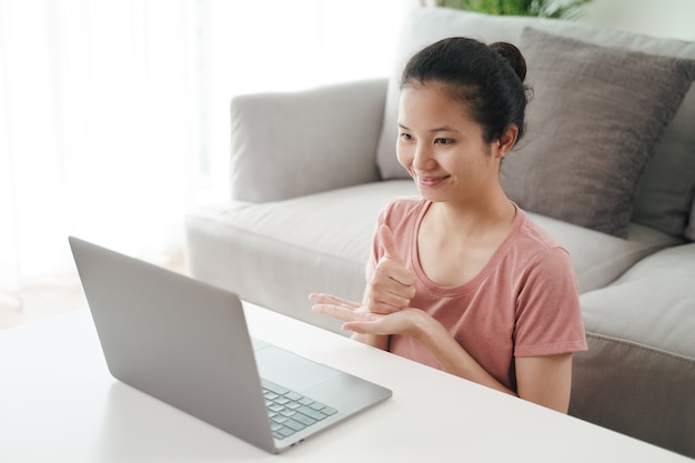 Jovem mulher asiática surda com deficiência usando computador portátil para aprendizagem de chamada de videoconferência online e comunicação em linguagem de sinais.