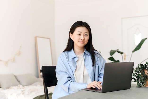 Jovem mulher asiática trabalhando em um laptop em casa e olhando para a câmera Conceito de negócios freelance