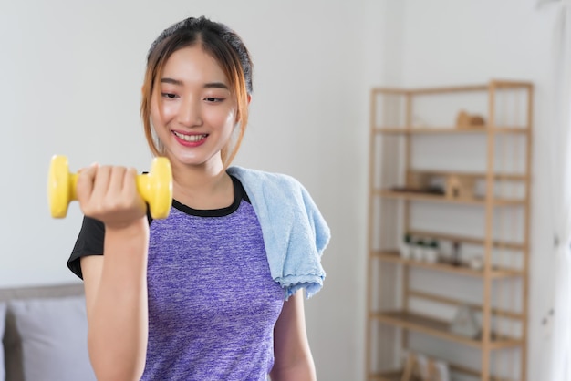 Jovem mulher asiática treinando e fazendo exercício para levantar halteres para um estilo de vida saudável em casa